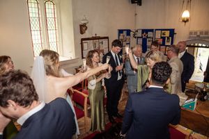 Wedding guests raising glasses in a toast inside a charming church venue with stained glass windows.