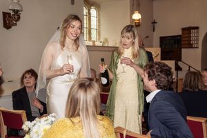 Bride in white gown and veil toasts with guest in green dress at intimate church wedding reception.