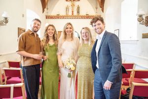 Wedding party posing in a church, bride in white holding bouquet, bridesmaid in green dress, guests in formal attire.