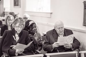 Black and white photo of wedding guests reading programs while seated in church pews during a ceremony.