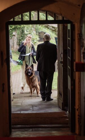 Woman with large dog greeting guests at church doorway during wedding.