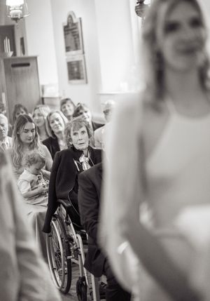 Black and white wedding photo of a woman in a wheelchair watching the bride walk down the church aisle.