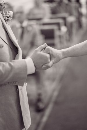 Close-up black and white photo of bride and groom holding hands during wedding ceremony in church.