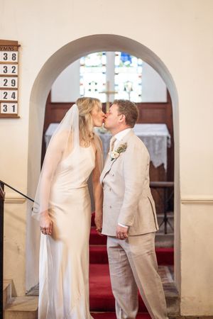 Bride and groom sharing a kiss under a stone arch inside a church after their wedding ceremony.