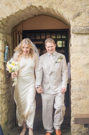 Joyful bride and groom exiting a stone church doorway holding hands after their wedding ceremony.