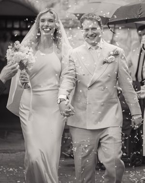 Bride and groom walk through confetti shower in black and white wedding photo.