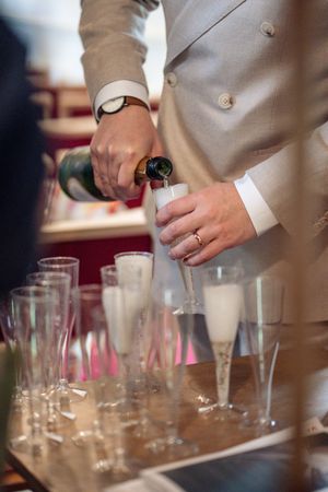 A man in a beige suit pours champagne into flute glasses at a wedding reception.