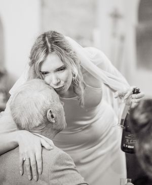 Black and white photo of a young blonde woman in a white dress embracing an older man at a wedding reception.
