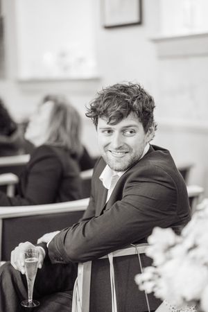 Smiling young man in a dark suit holding a champagne flute at a wedding reception.