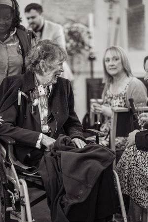 Elderly guest in wheelchair laughing at a wedding reception in black and white photo.