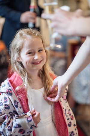 Happy young flower girl smiling at wedding reception holding adult's hand.