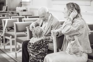 Elderly man interacting with a child in church pews while a woman looks on in black and white photo.