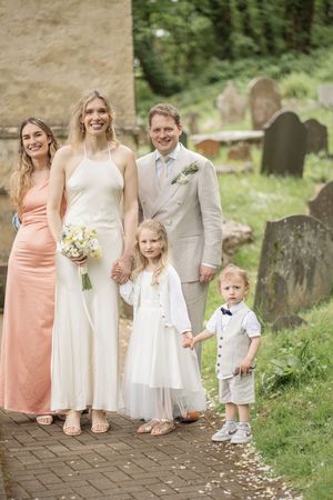 Wedding party with bride, groom, bridesmaid, flower girl, and page boy posing outside a church.