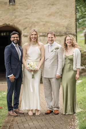 Happy wedding couple posing with two guests outside a stone church on their special day.