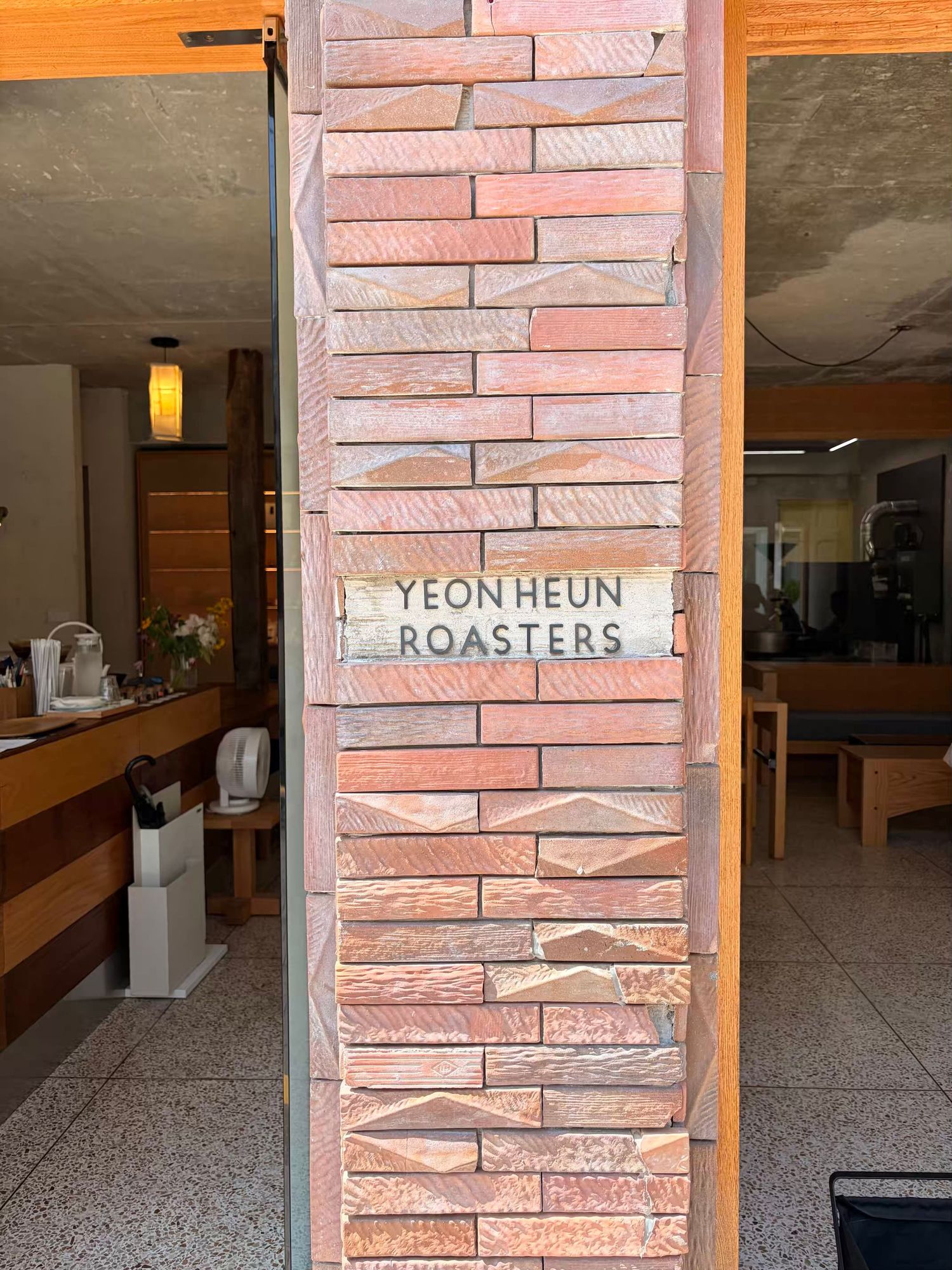 Yeon Heun Roasters coffee shop entrance with rustic red brick column signage in a warm, inviting cafe interior.