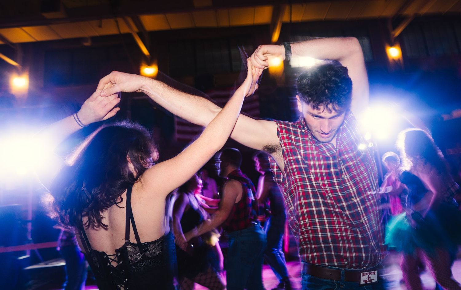Couple dancing energetically under colorful stage lights at a lively indoor dance event. Rustic Wedding Photographers Helena Montana.