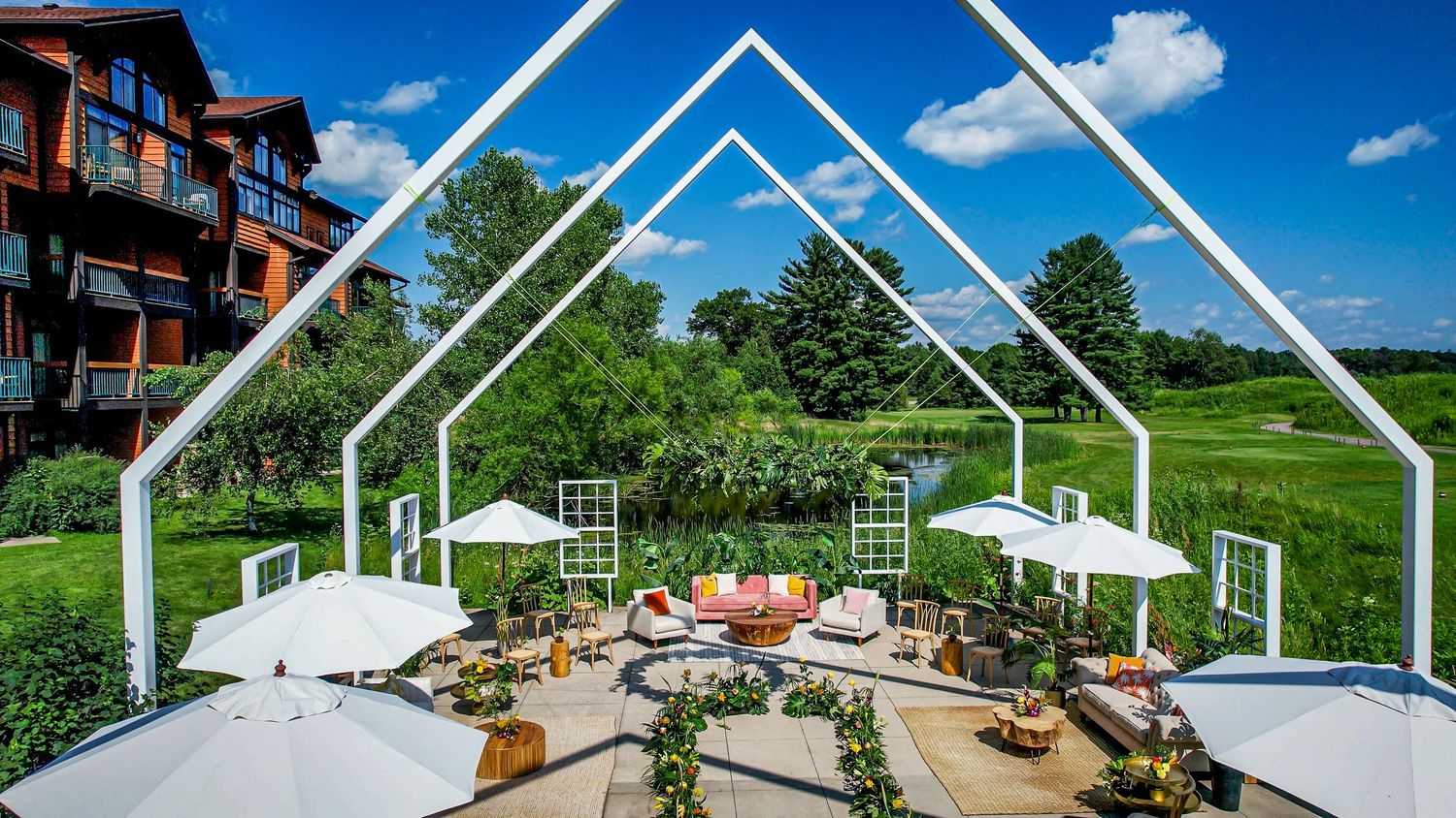 Elegant outdoor patio with white geometric arch frames, umbrellas, and lush green golf course backdrop.