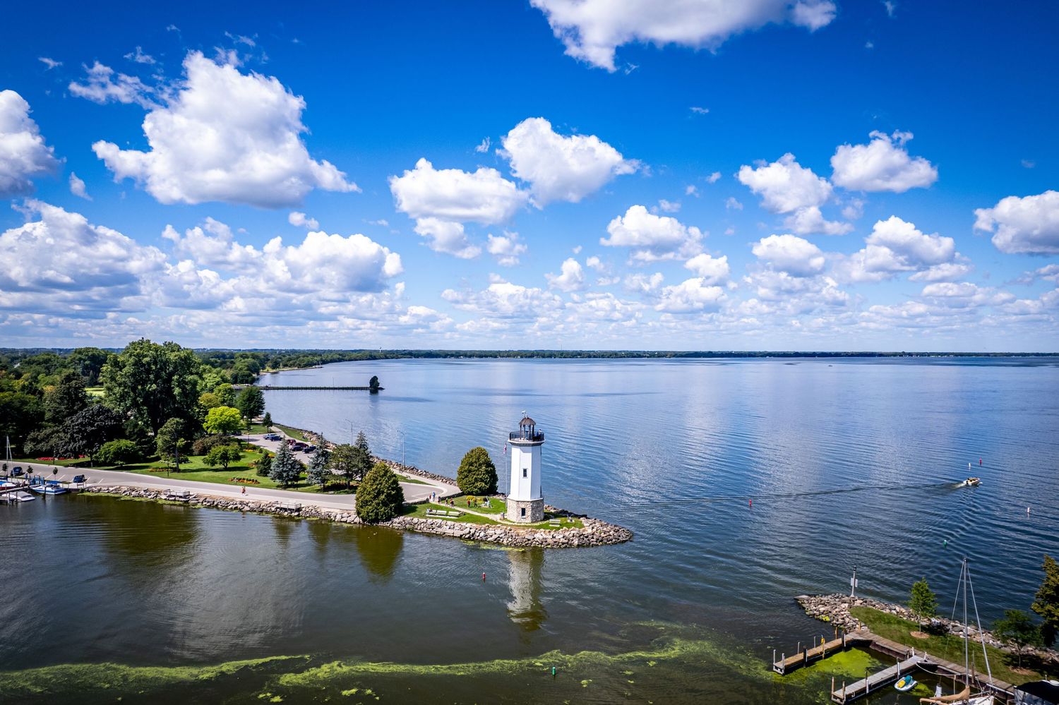 Aerial view of a white lighthouse on a rocky peninsula surrounded by calm blue lake waters.