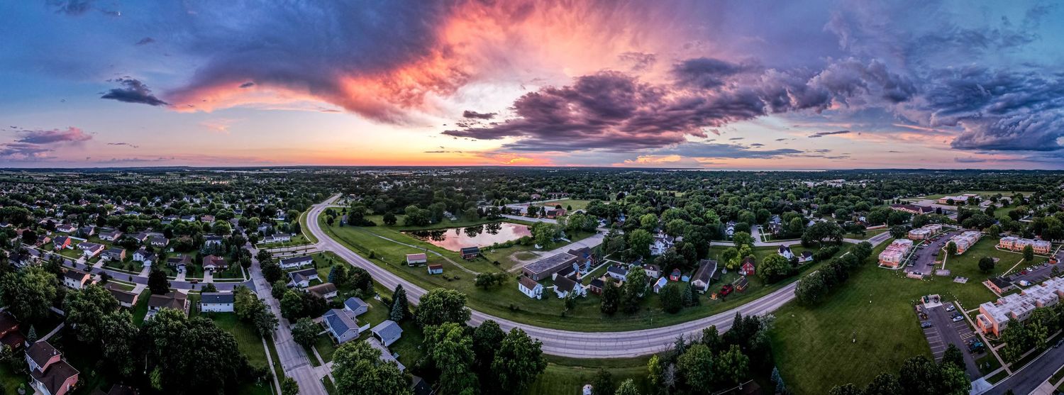 Dramatic panoramic aerial sunset over a suburban neighborhood with vibrant pink and purple storm clouds.
