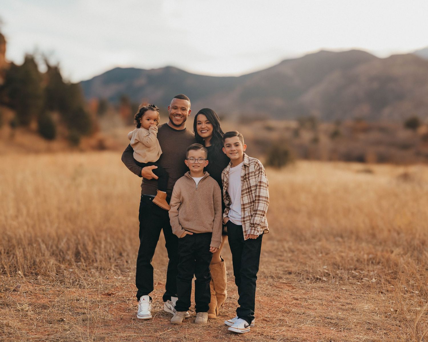 Family of five posing in a golden field with mountain backdrop during autumn sunset photography session.
