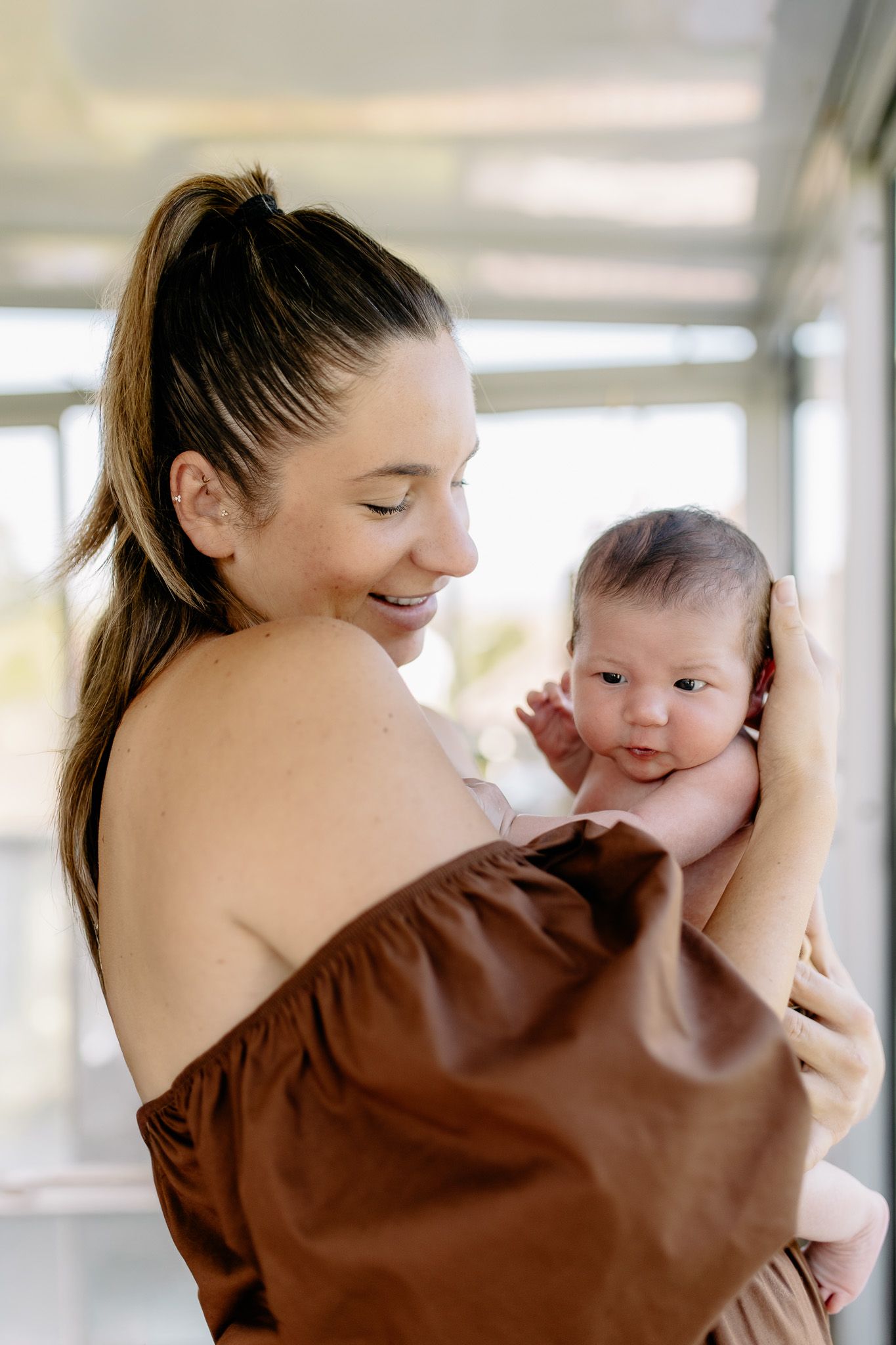 Maman avec une robe aux manches bouffantes arrivant en bas des épaules teinte marron chocolat, qui sourit à son bébé nouveau-né