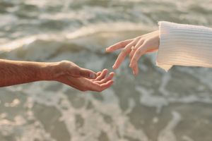 Two hands reaching toward each other over ocean waves, symbolizing connection and love.