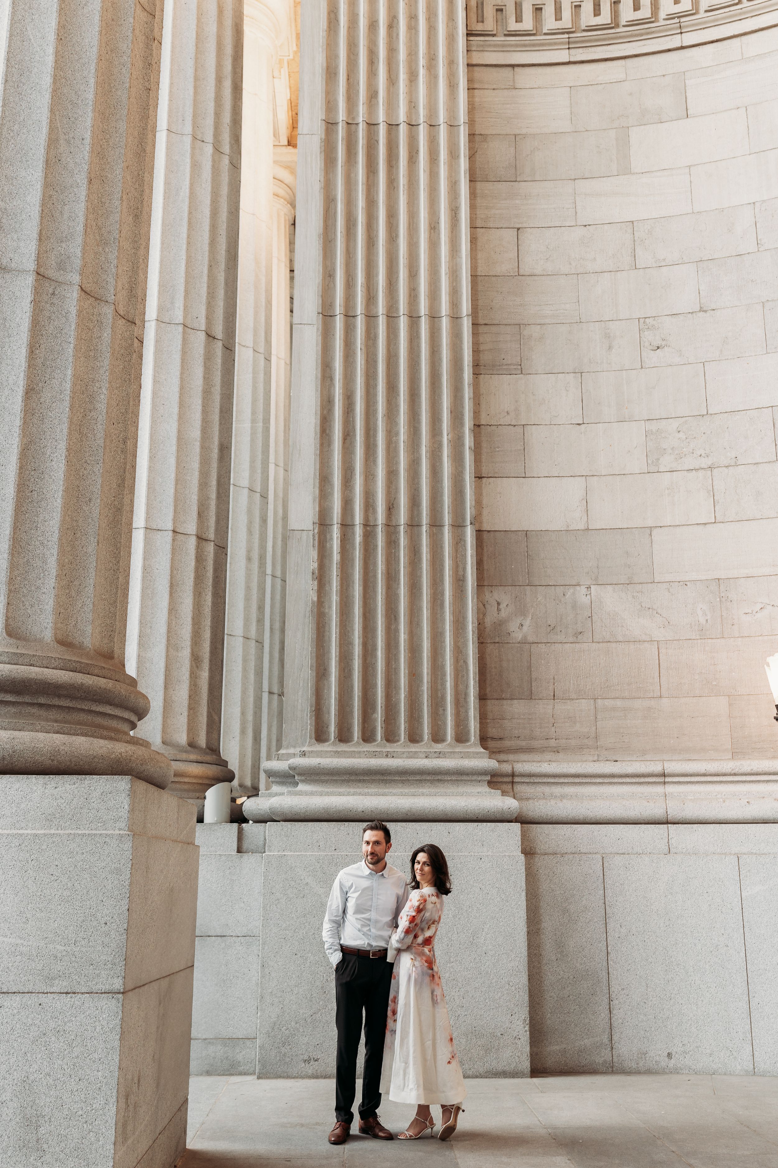 Couple standing between grand stone columns at the Lincoln Memorial in Washington DC during an engagement photo session.