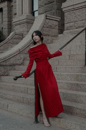 Woman in stunning red pleated maxi dress posing on grand stone steps with iron railing.