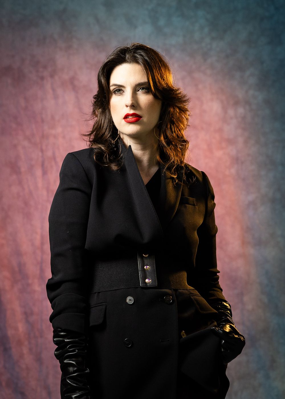 Dramatic fashion portraits featuring black coat and red lipstick against mottled backdrop.
