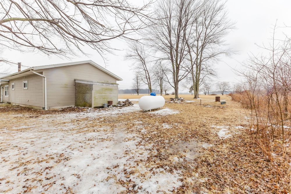 Snowy backyard with detached garage, propane tank, and bare winter trees on rural property.