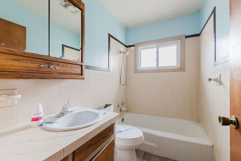 Vintage bathroom with tiled walls, wood vanity, mirror cabinet, tub-shower combo, and window.