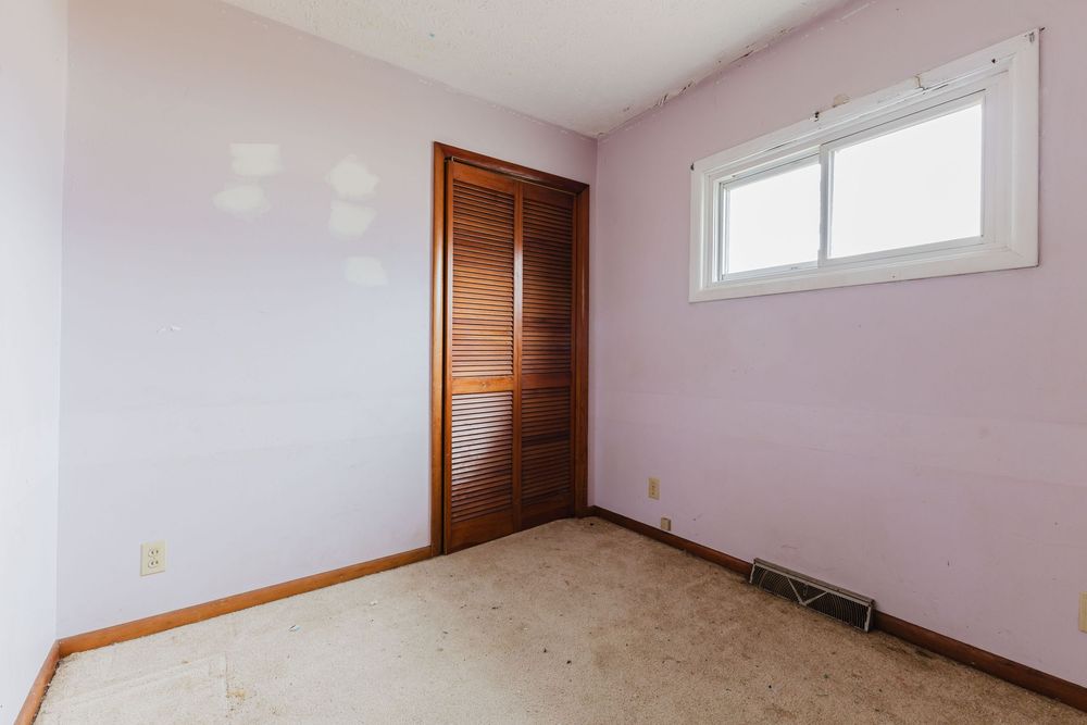 Small bedroom with lavender walls, wood closet doors, carpeted floor, and single window.