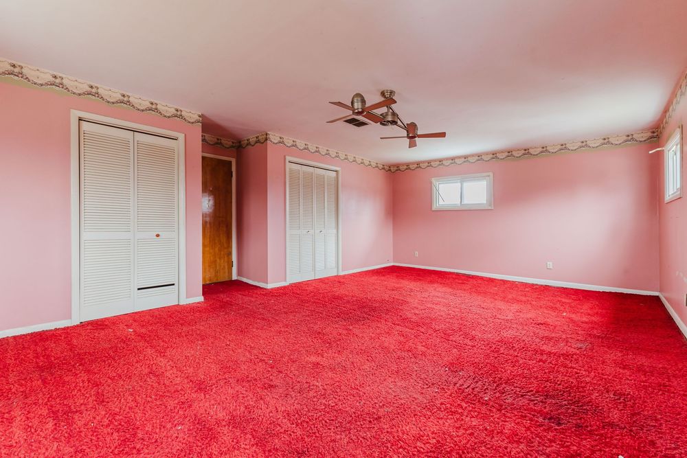 Bright pink bedroom with red carpet, ceiling fan, two closets, and decorative border trim.