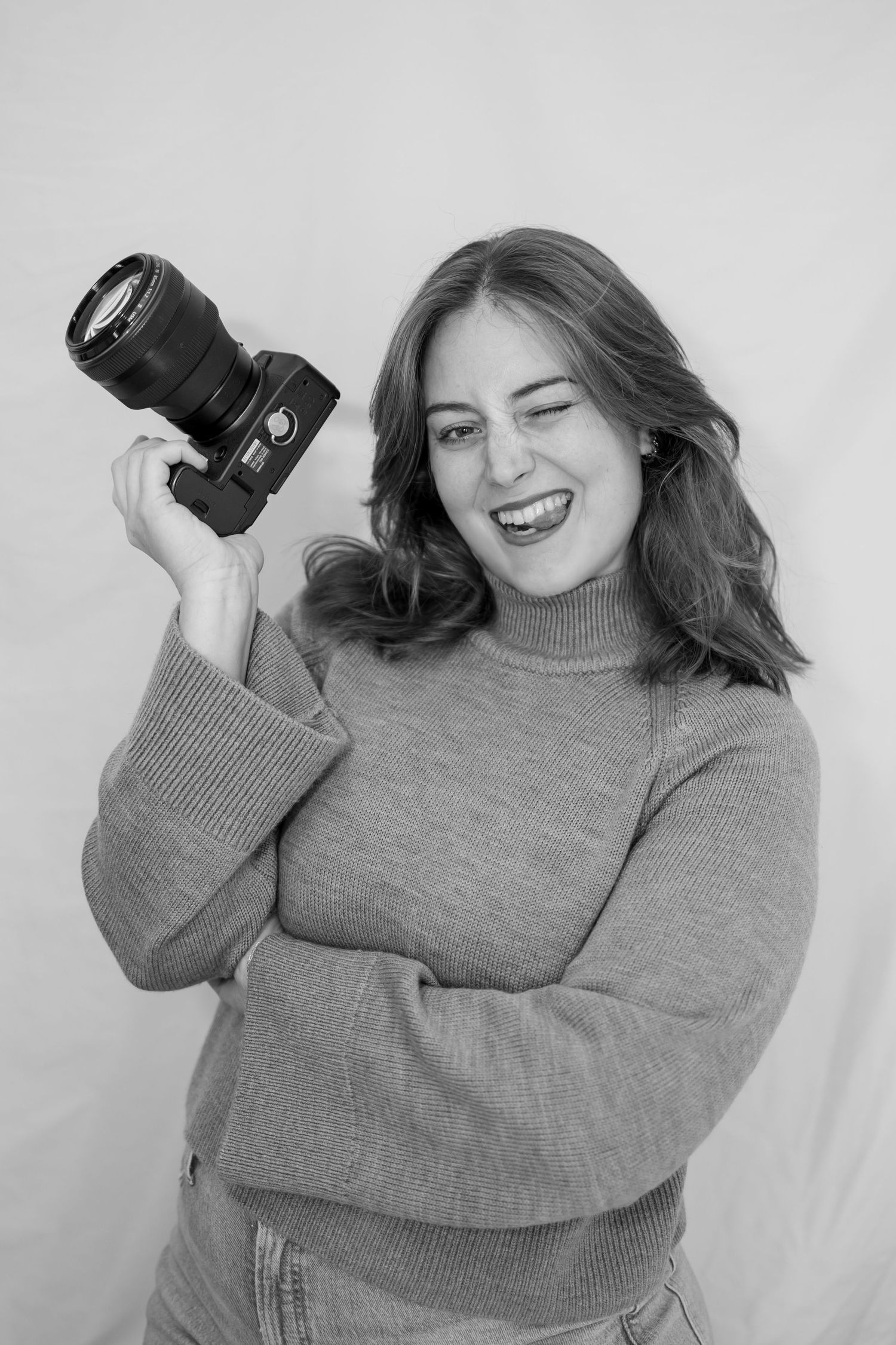 A series of four black and white photos showing someone in a gray sweater posing playfully with a camera.