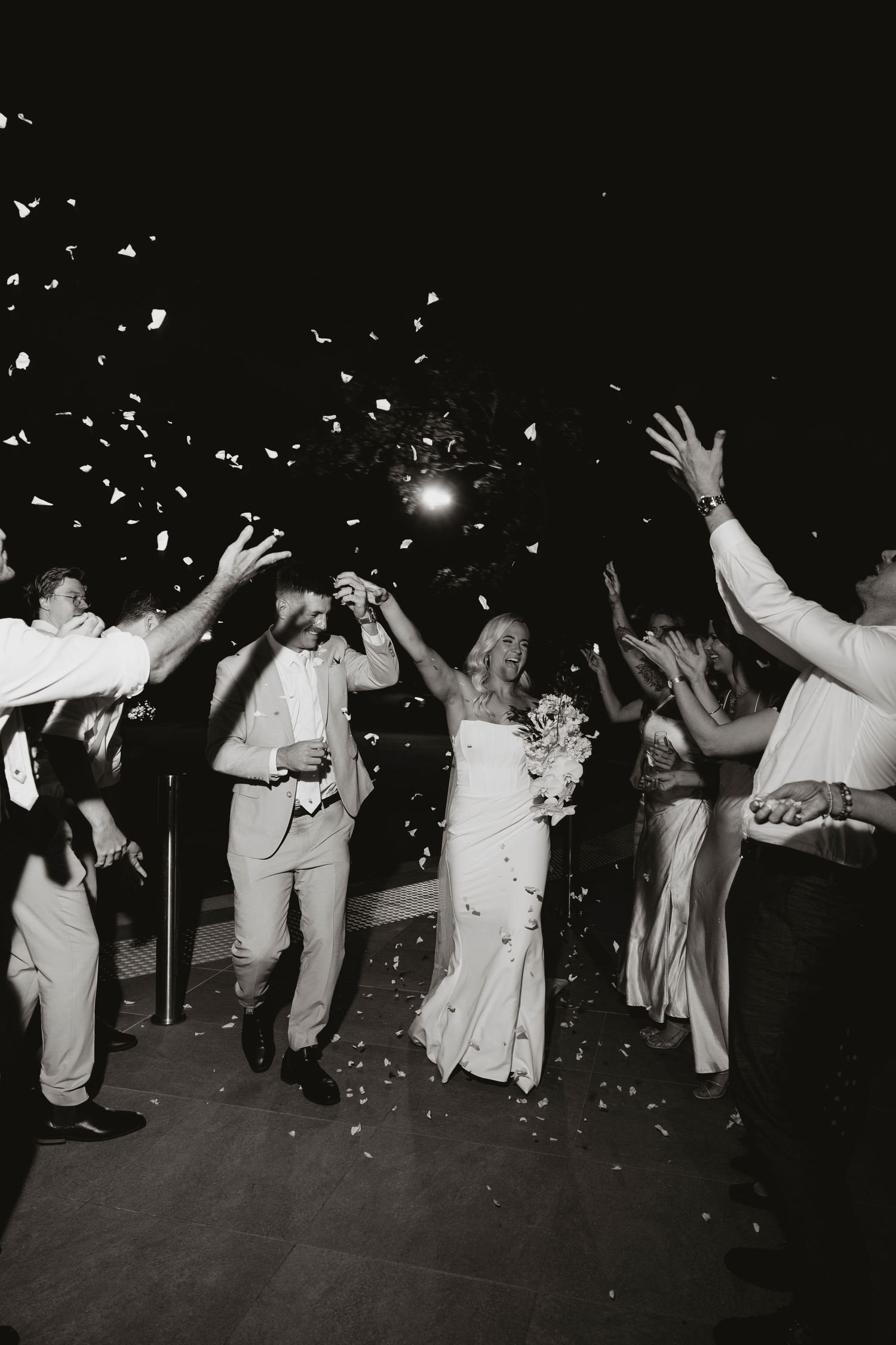 Wedding party celebrates with confetti toss during black and white reception exit moment.