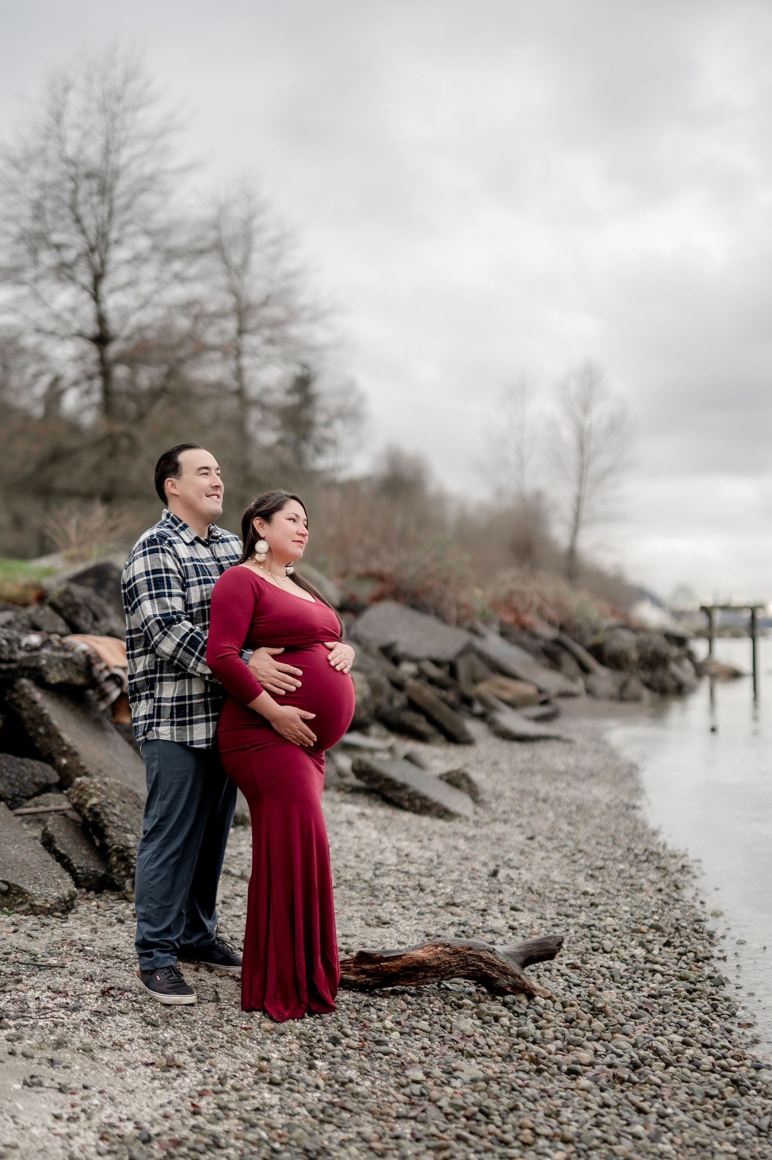 A couple in casual attire embraces on a rocky beach shoreline on an overcast day.