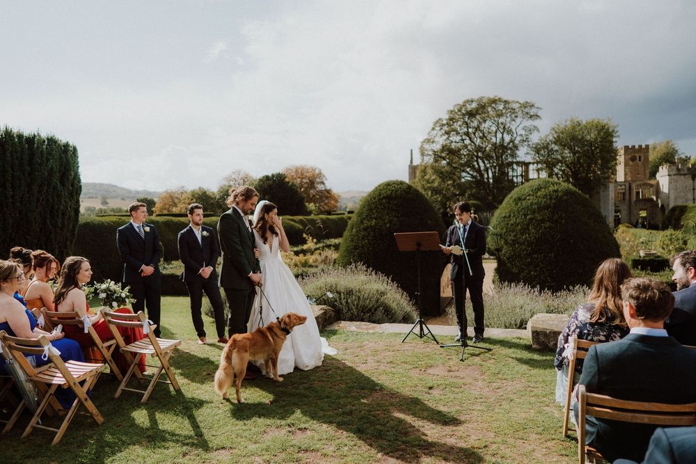 Panoramic view of wedding guests seated on wooden chairs in a garden setting.