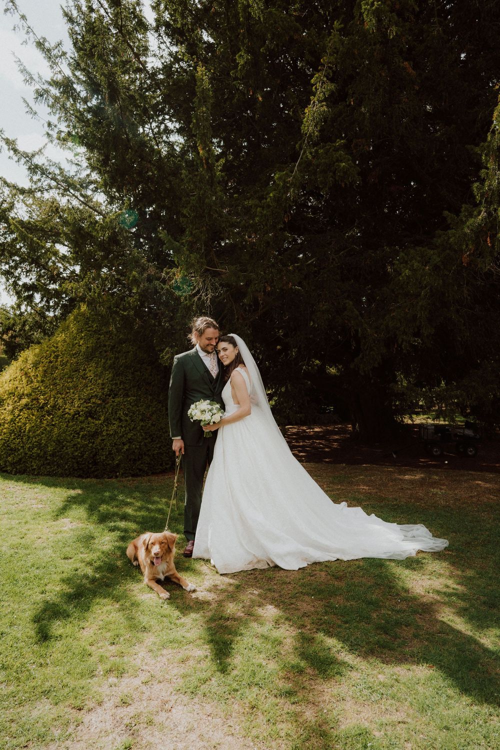 A couple shares a romantic moment on a grassy lawn with their dog sitting nearby.