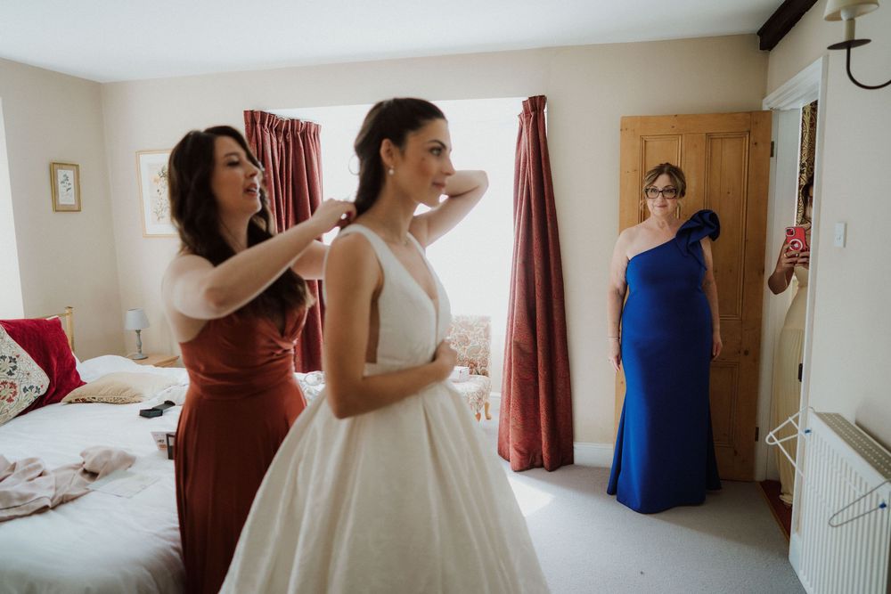 A wedding preparation scene with attendants helping with final dress adjustments.