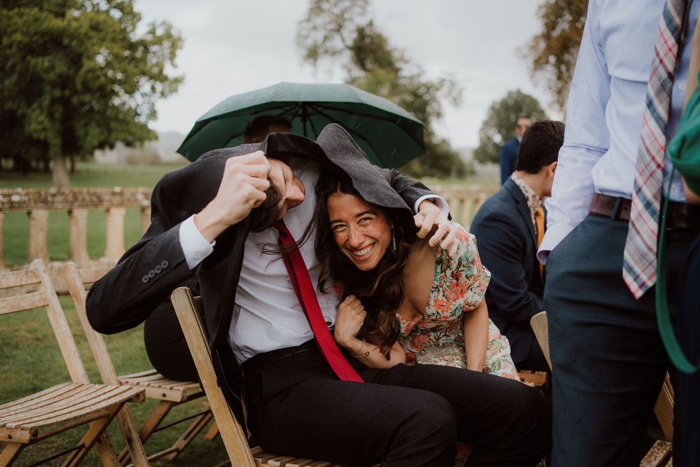 Wedding guests share joyful moments while seated on wooden chairs during an outdoor celebration.