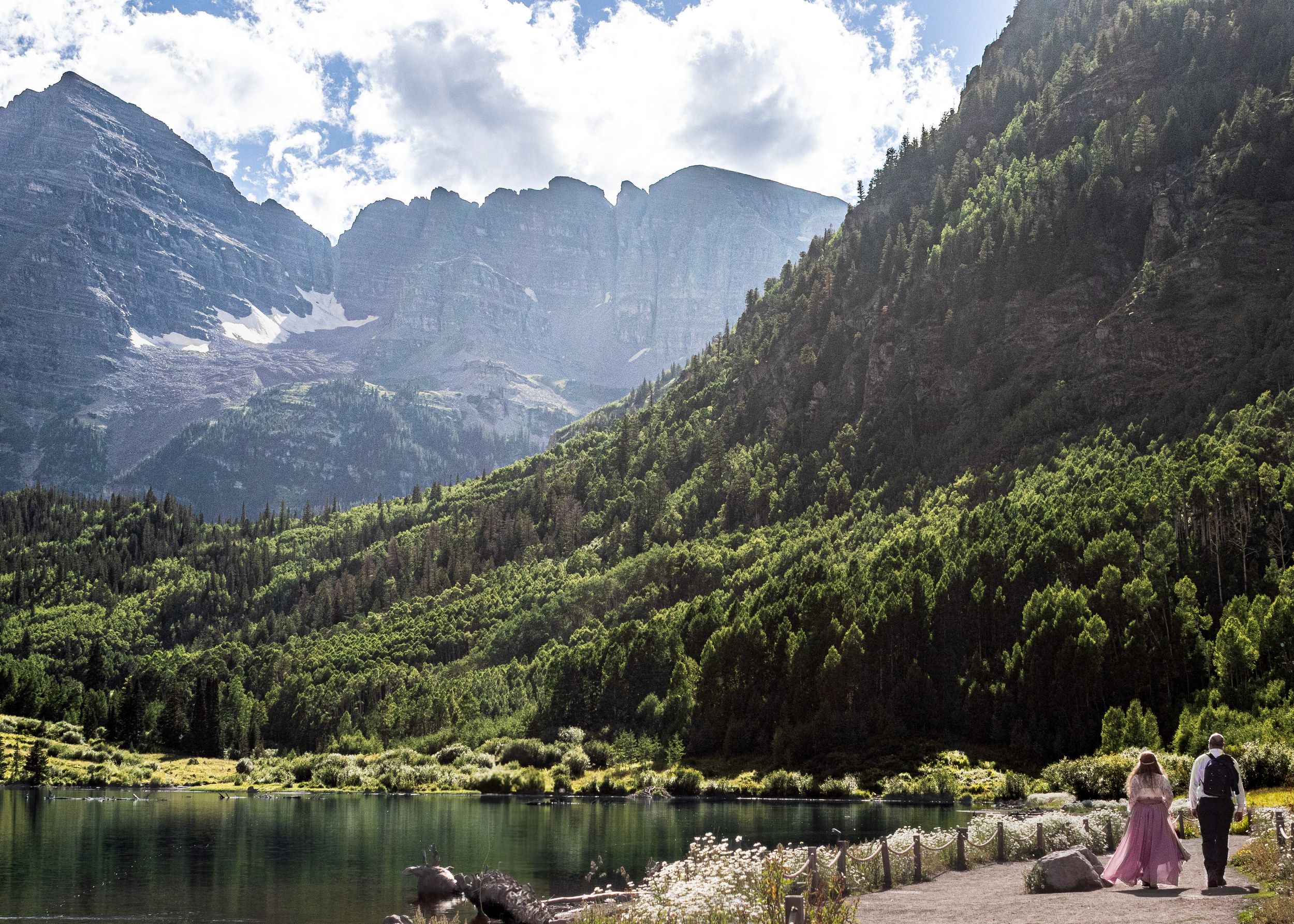 Alpine lake surrounded by towering mountains and lush green forests on a summer day.