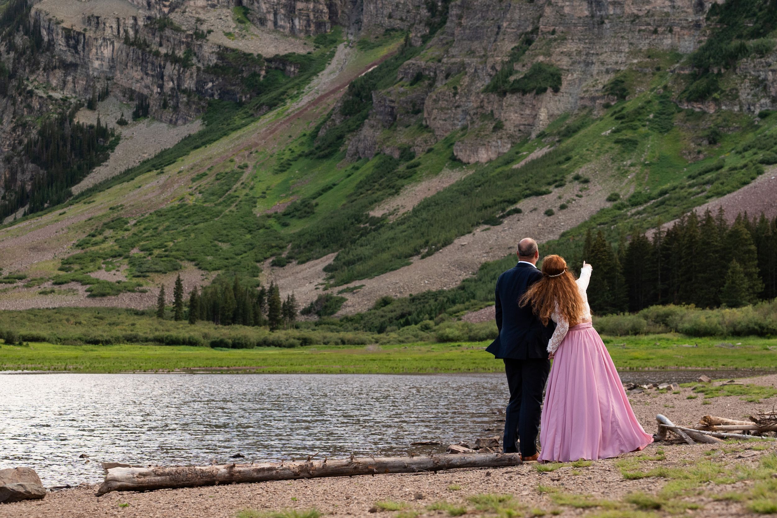 Scenic mountain valley with rocky cliffs and green meadows beside a tranquil lake.