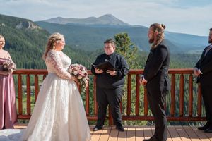 Couple celebrates their wedding ceremony on a wooden deck overlooking majestic mountain ranges.