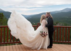 Wedding dress train flows across wooden deck with mountain vista in background.