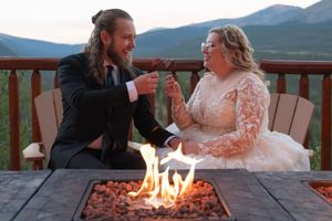 Couple sits by fire pit during mountain wedding celebration with scenic backdrop.