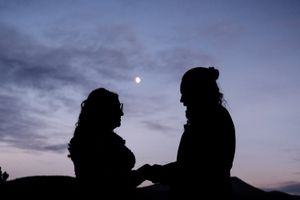 Silhouettes of wedding couple against dusky mountain sky.