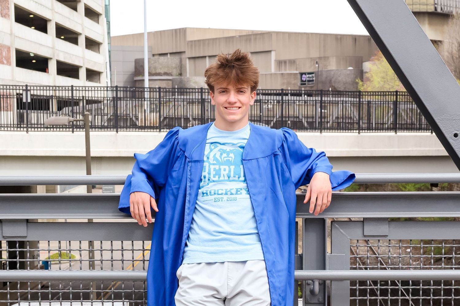 Person in blue jacket posing against urban architecture and metal railings.