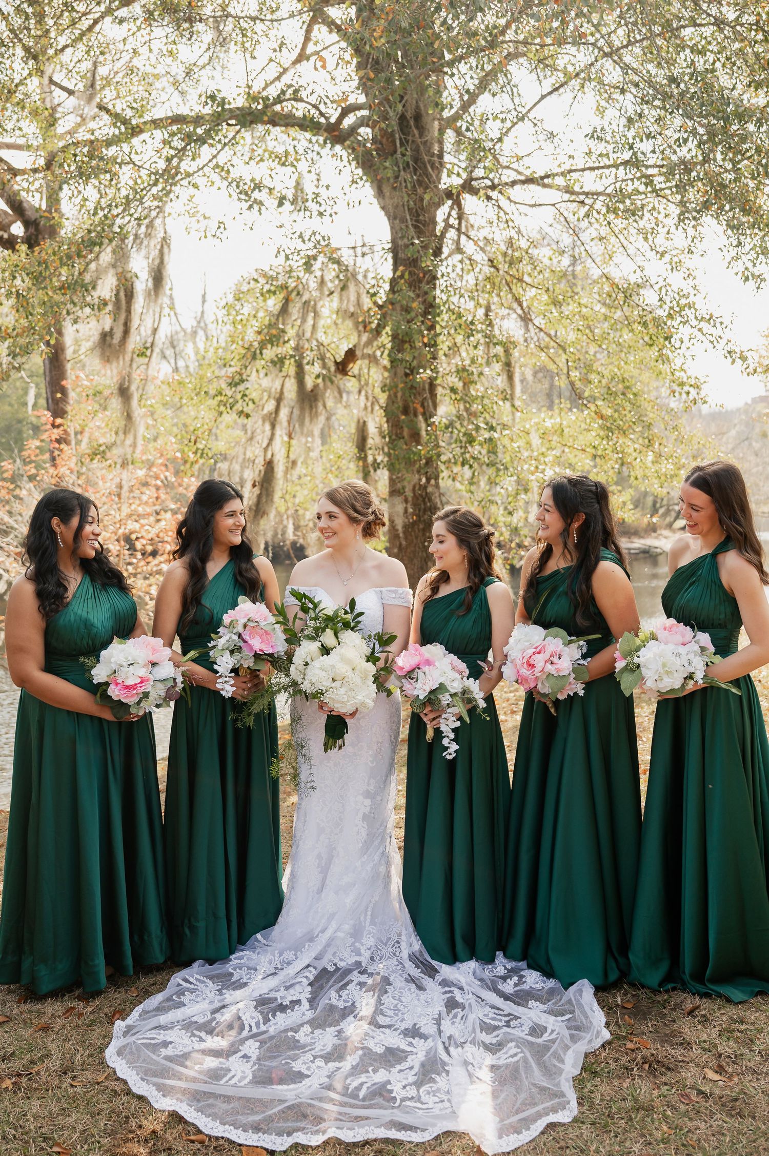 Wedding party in emerald green dresses and white gown pose together outdoors.
