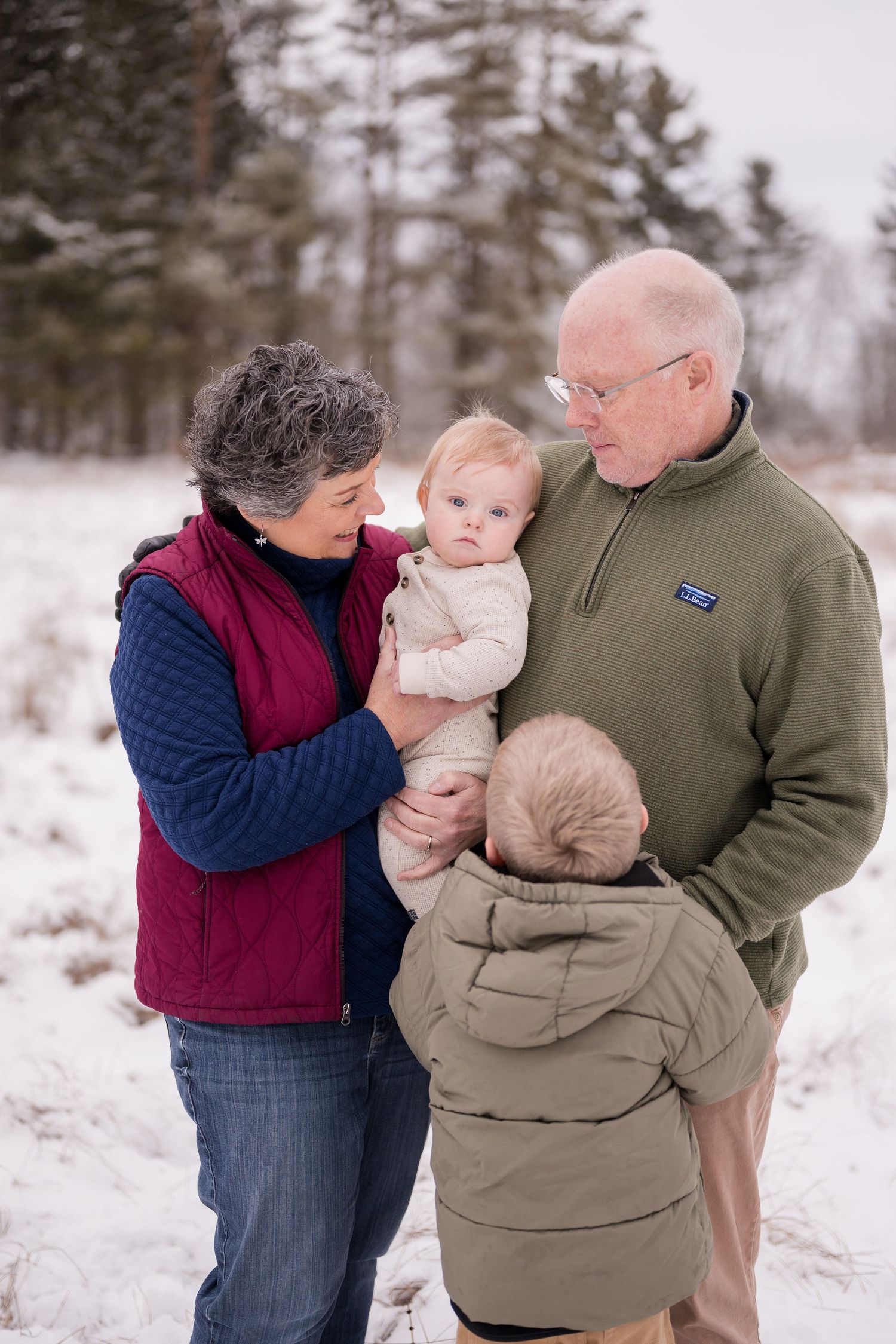 Family portrait session in snowy winter landscape with pine trees.