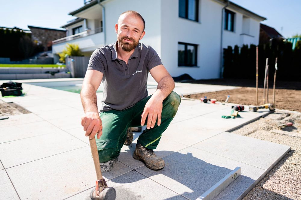 Landscaper carefully measuring and laying stone pavers in backyard construction project.